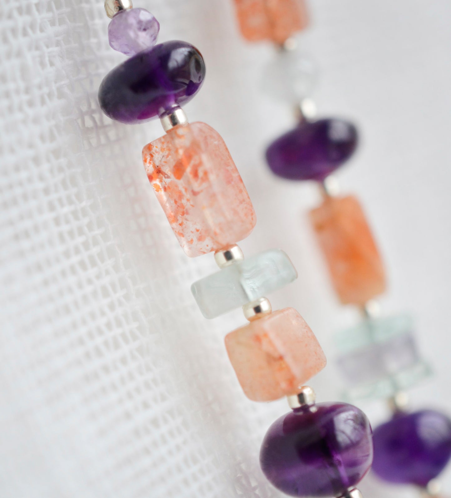 Mismatched gemstone long bar earrings shown in sterling silver. Stones include: amethyst, aquamarine, fluorite, and sunstone. Stones are set onto a long straight bar. Close up image.