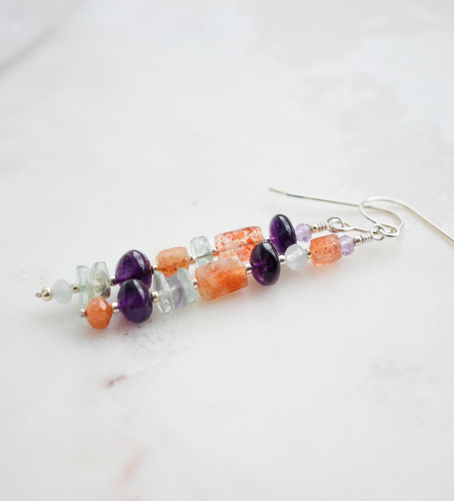Mismatched gemstone long bar earrings shown in sterling silver. Stones include: amethyst, aquamarine, fluorite, and sunstone. Stones are set onto a long straight bar.