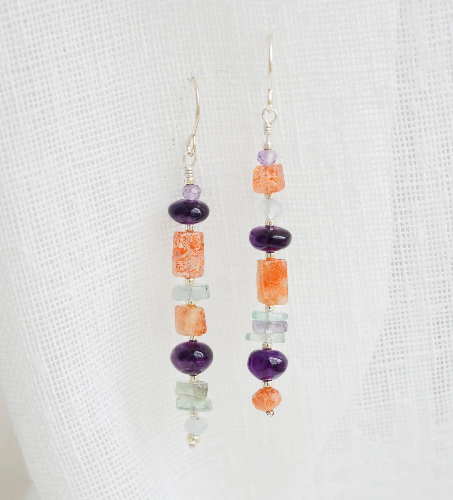 Mismatched gemstone long bar earrings shown in sterling silver. Stones include: amethyst, aquamarine, fluorite, and sunstone. Stones are set onto a long straight bar.