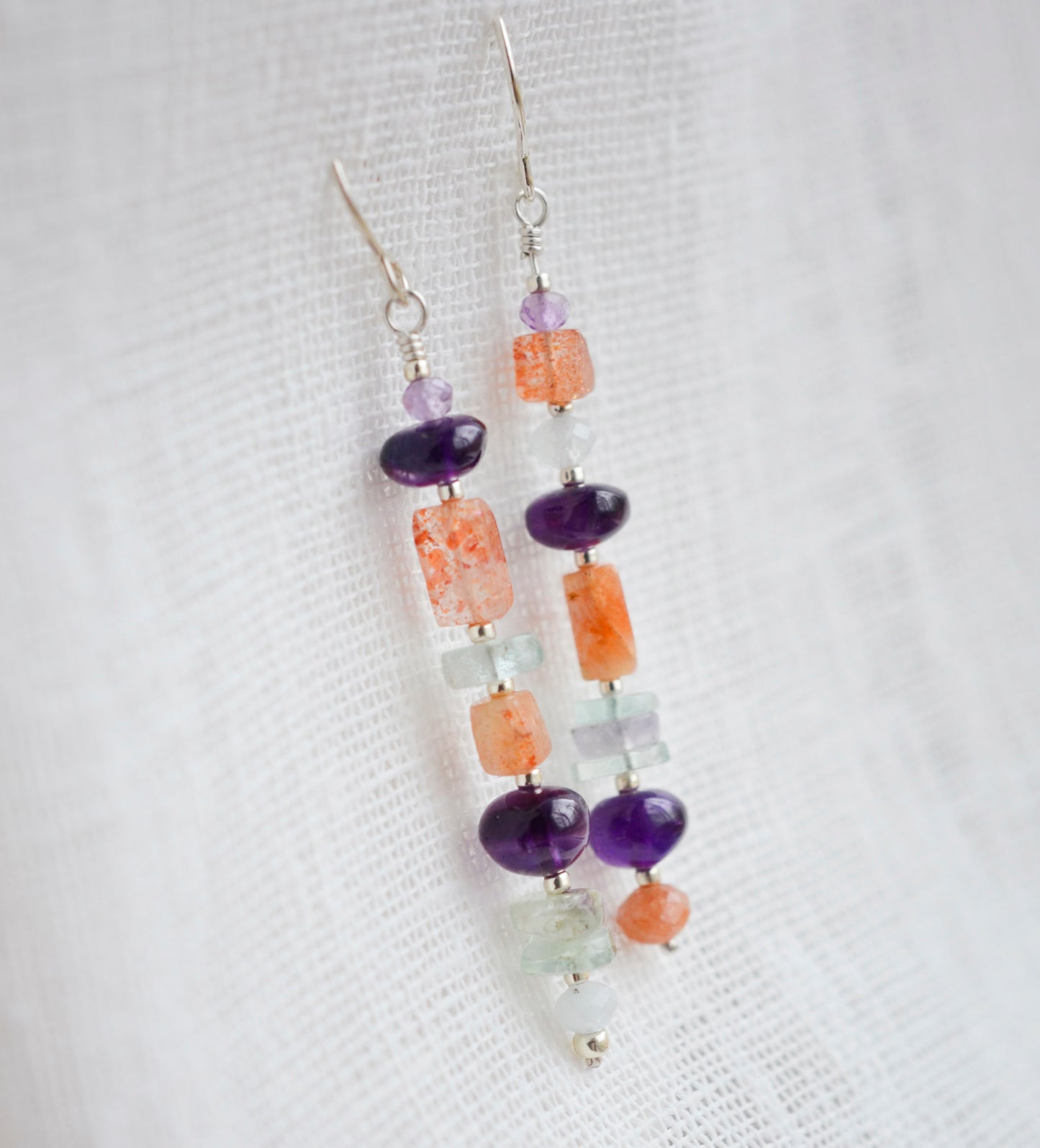 Mismatched gemstone long bar earrings shown in sterling silver. Stones include: amethyst, aquamarine, fluorite, and sunstone. Stones are set onto a long straight bar.