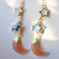 Mother of pearl, Labradorite, and Peach Moonstone moon and star dangle earrings in gold. Each earring has two stars hanging over a peach moonstone crescent. Close up image.