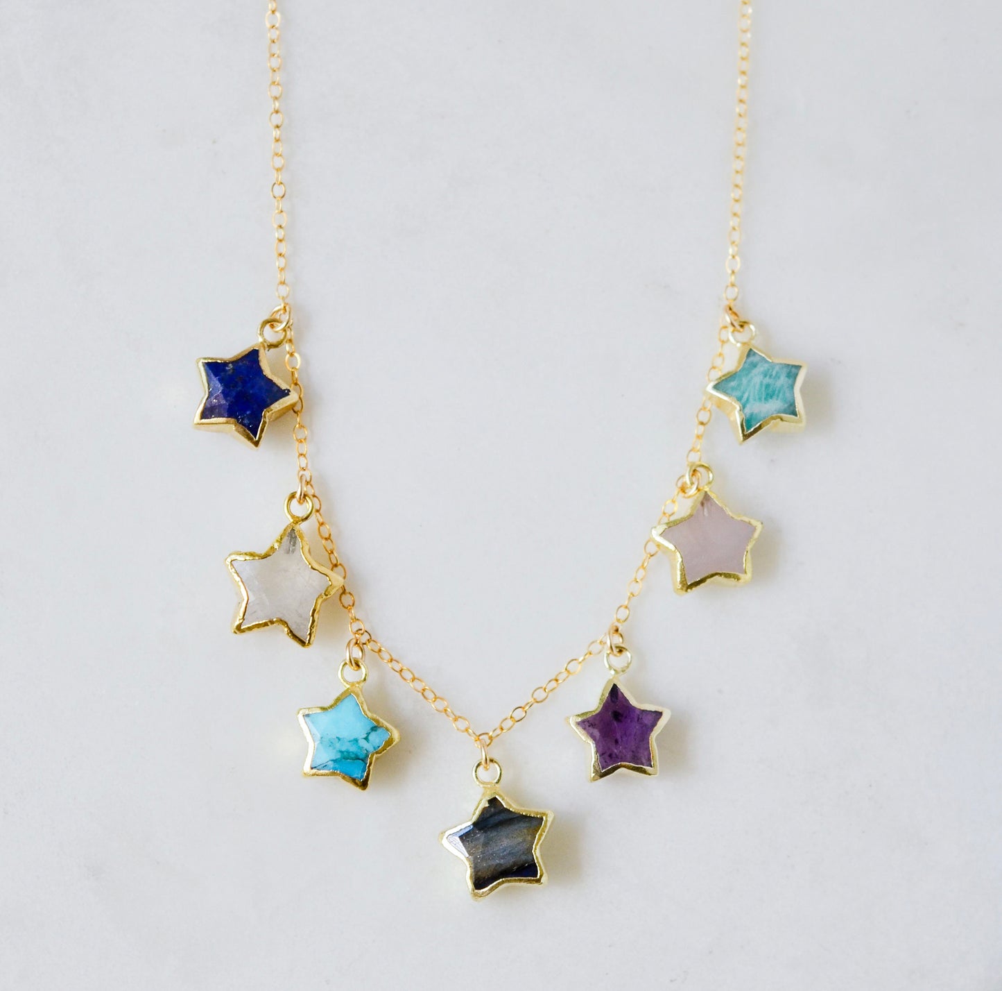 Necklace with star-shaped charms on a 14k gold filled chain. Each star is a different gemstone. Stones include: Lapis lazuli, rainbow moonstone, turquoise, labradorite, amethyst, rose quartz, and amazonite. This necklace is handmade in Connecticut by Gemnia.
