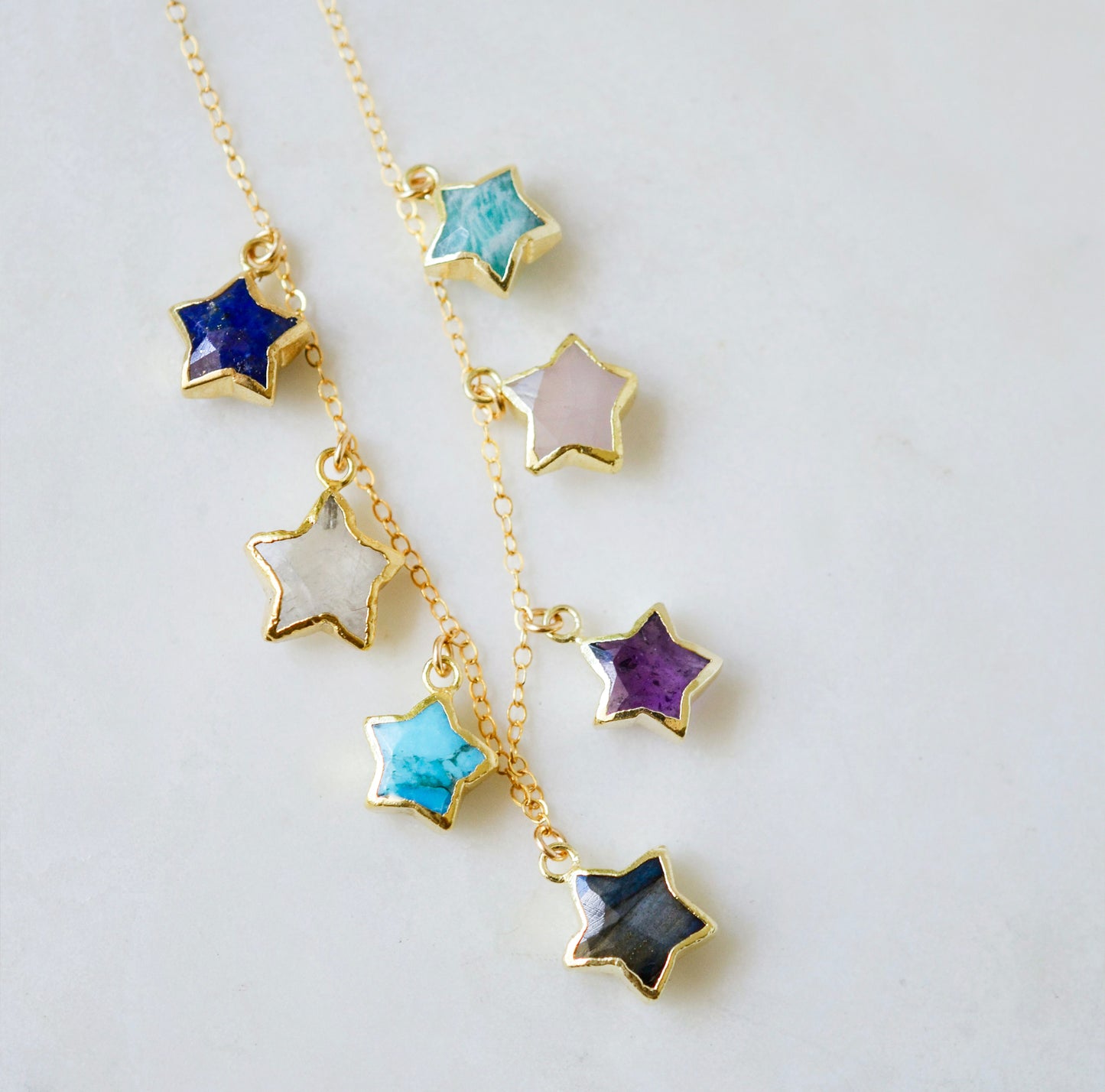 Necklace with star-shaped charms on a 14k gold filled chain. Each star is a different gemstone. Stones include: Lapis lazuli, rainbow moonstone, turquoise, labradorite, amethyst, rose quartz, and amazonite. This necklace is handmade in Connecticut by Gemnia.