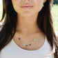 A woman wearing a handmade 14k gold filled necklace of seven stars. Each star is a different gemstone. Stones include: Lapis lazuli, rainbow moonstone, turquoise, labradorite, amethyst, rose quartz, and amazonite.