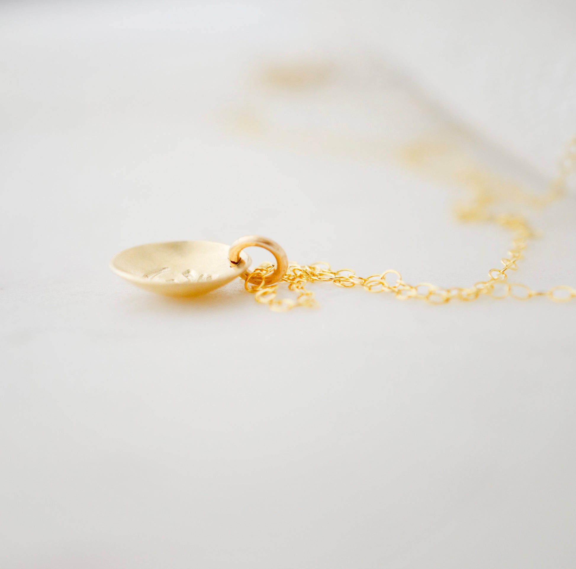 Om symbol stamped into a circle disc and put on a gold filled chain. Side view.