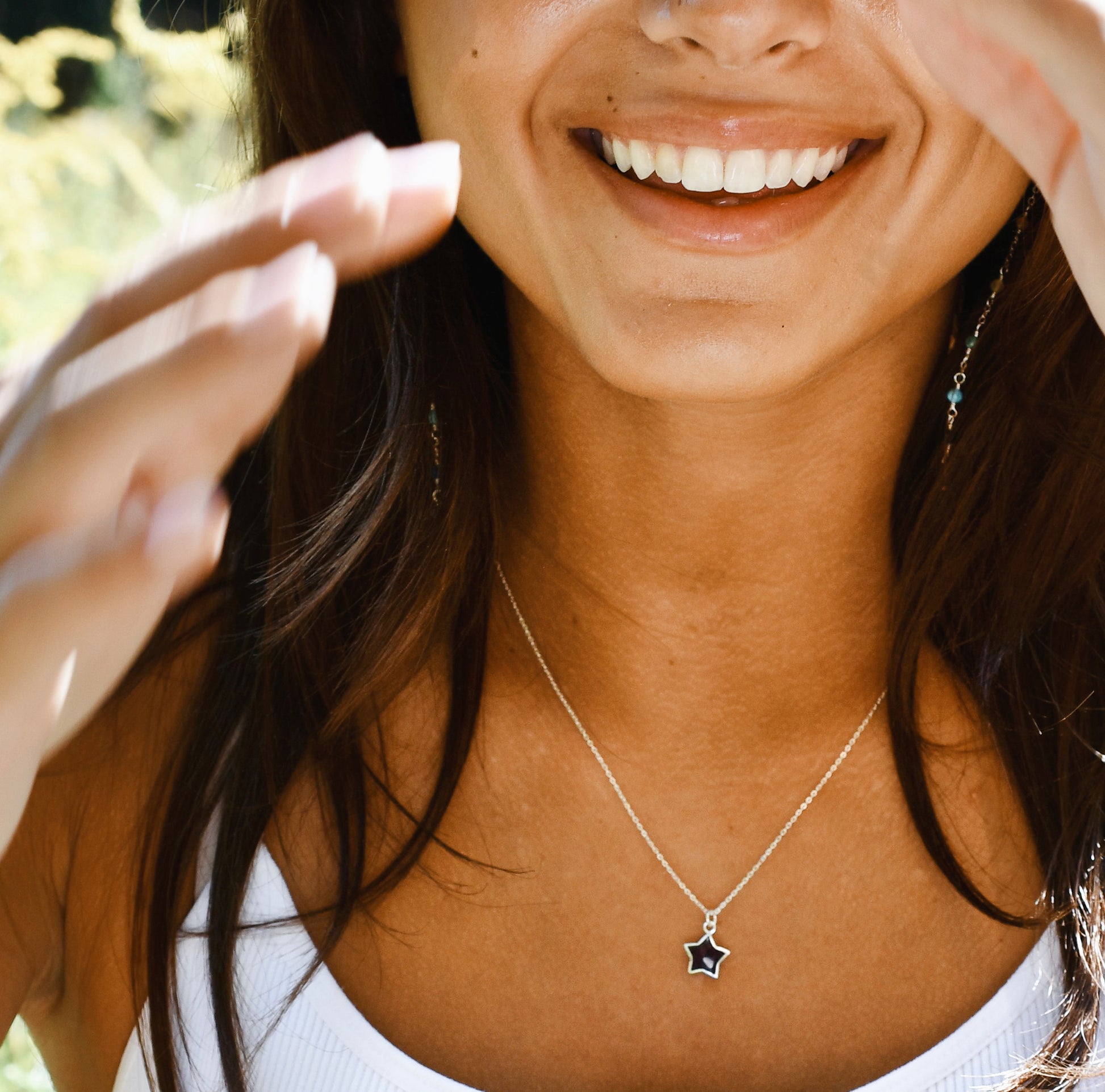 Woman wearing a necklace with a star pendant, outdoors. Modeled in sterling silver.