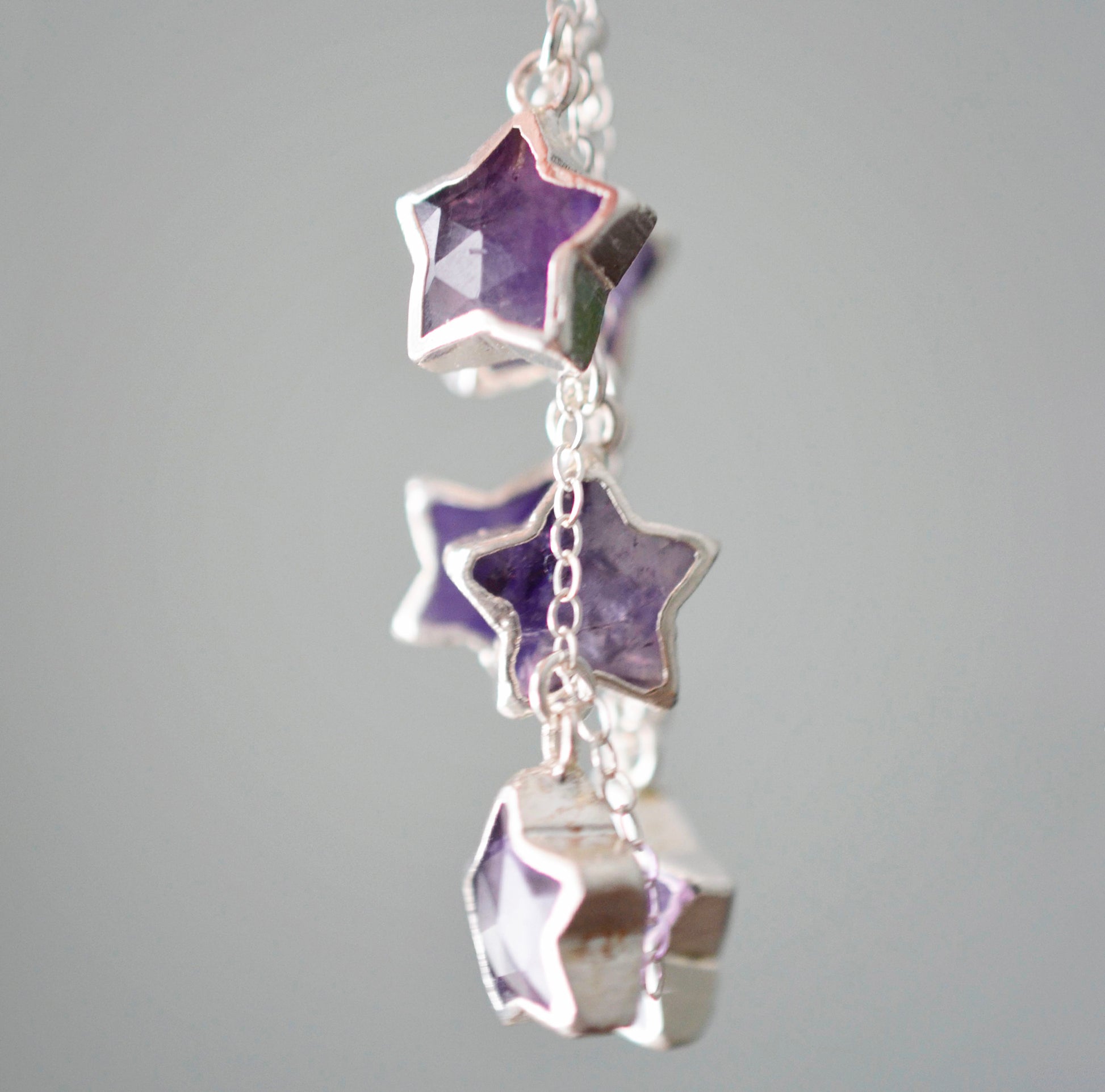 Sterling silver celestial amethyst star earring jewelry. Each earring features three purple amethyst stars dangling from a sterling silver chain. Close up image.
