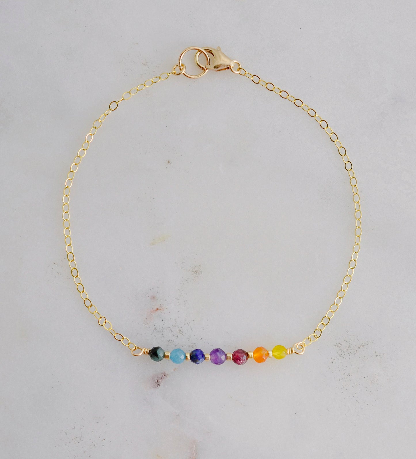 A dainty, minimalist chakra pride beaded chain bracelet handmade with small natural gemstones in rainbow colors. 
