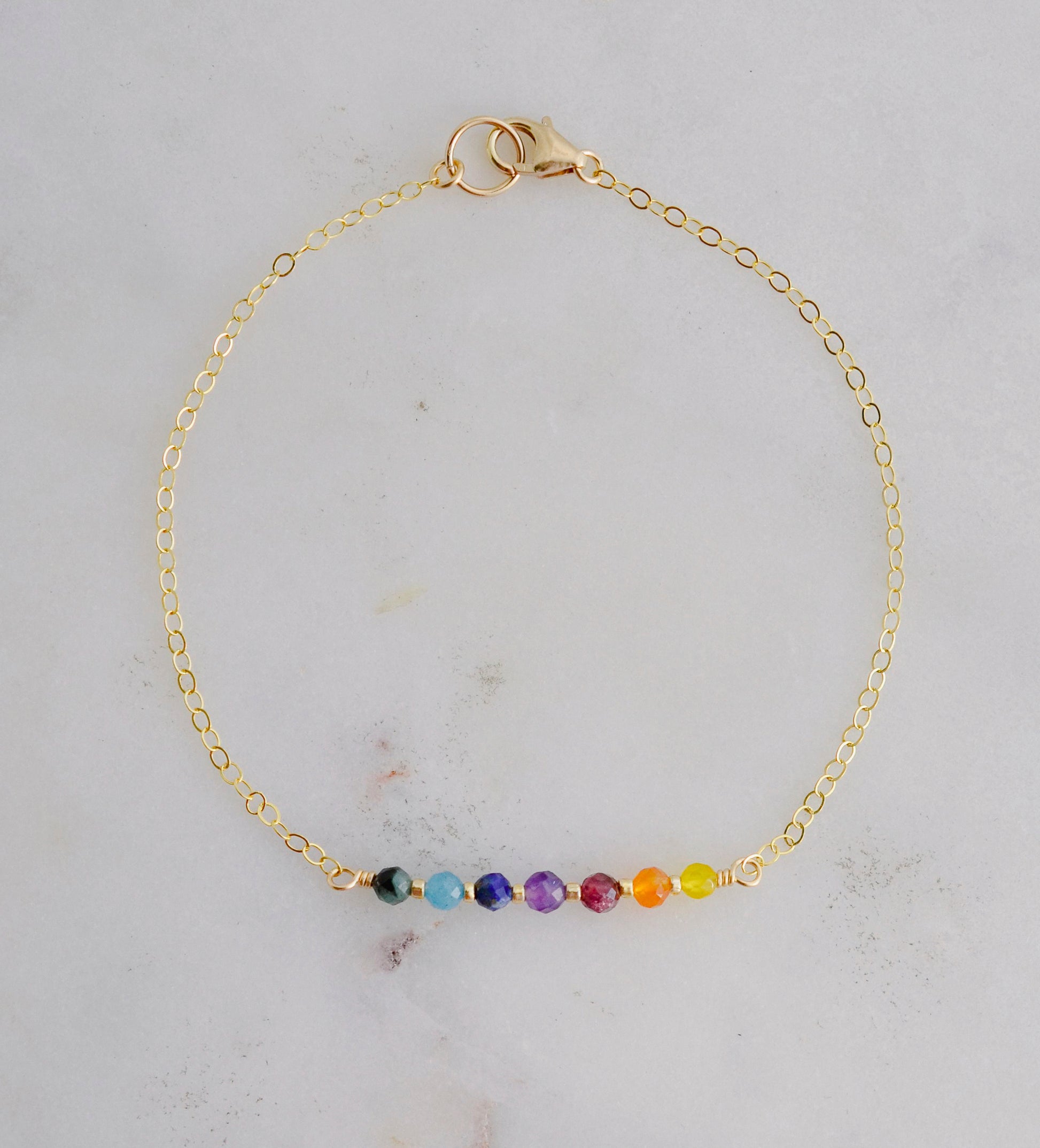 A dainty, minimalist chakra pride beaded chain bracelet handmade with small natural gemstones in rainbow colors. 