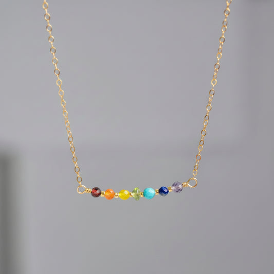 A dainty, minimalist rainbow, chakra, or pride necklace handmade with natural crystals that are arranged on a bar in the order of the rainbow. All of our jewelry is handmade in Connecticut.