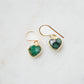 Raw emerald heart earrings in gold. The stones are bezeled in 22k gold then set on gold earwires. The gemstone colors range in dark greens with hints of white or black.