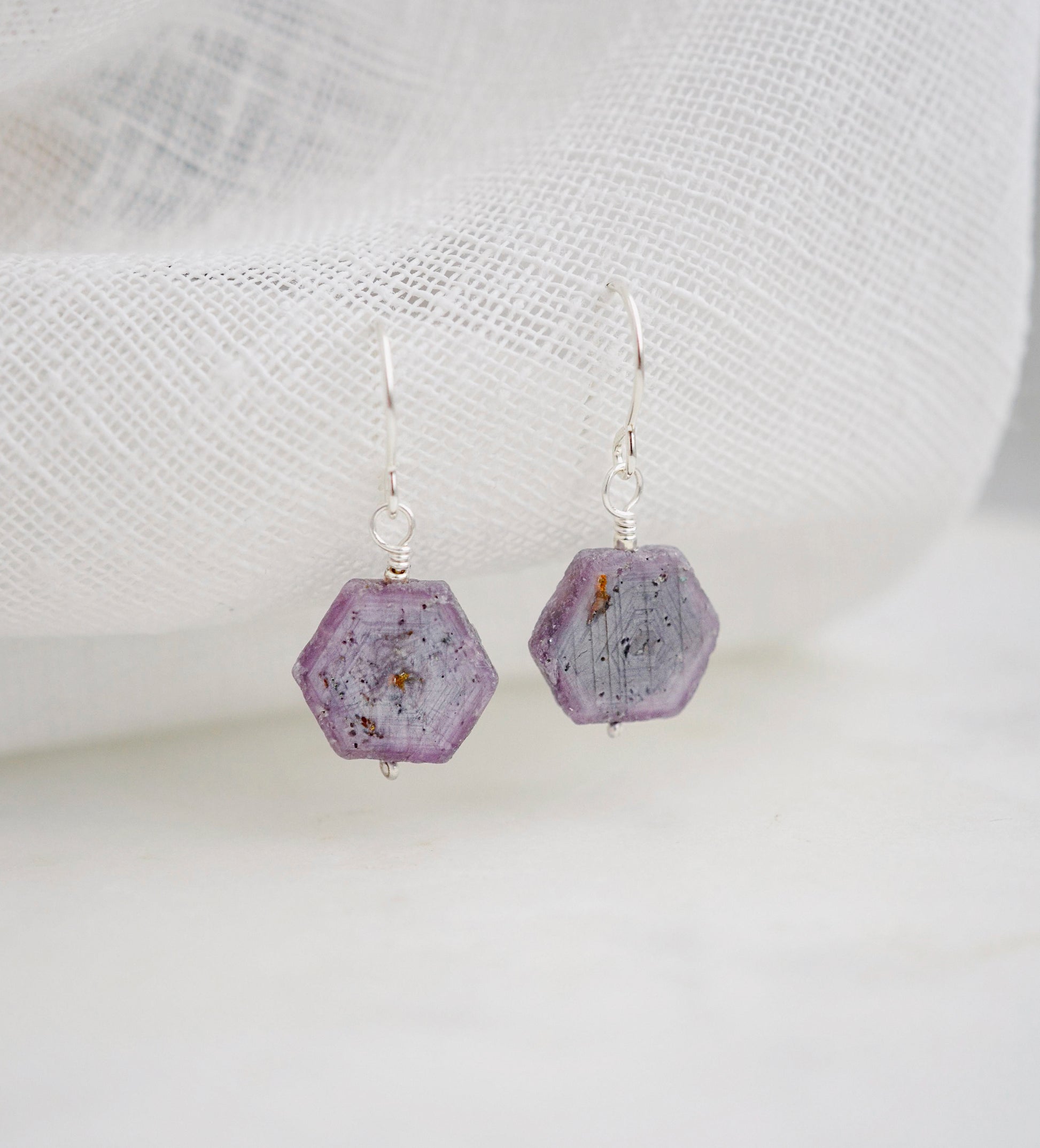 Purple-pink raw ruby stones suspended from sterling silver earwires. The stones are rough and in their natural hexagonal shape. 