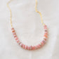 Natural pink Rhodochrosite beaded handmade necklace shown in 14k gold filled. The gemstones vary in shades of pink, peach, white, and gray and are faceted rondelle shape. They span approximately 4 inches across the front of the necklace, then attach to a dainty cable chain. Also available in sterling silver.