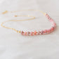 Natural pink Rhodochrosite beaded handmade necklace shown in 14k gold filled. The image is a size view showing the dainty metal beads. The gemstones vary in shades of pink, peach, white, and gray and are faceted rondelle shape. They span approximately 4 inches across the front of the necklace, then attach to a dainty cable chain. Also available in sterling silver.