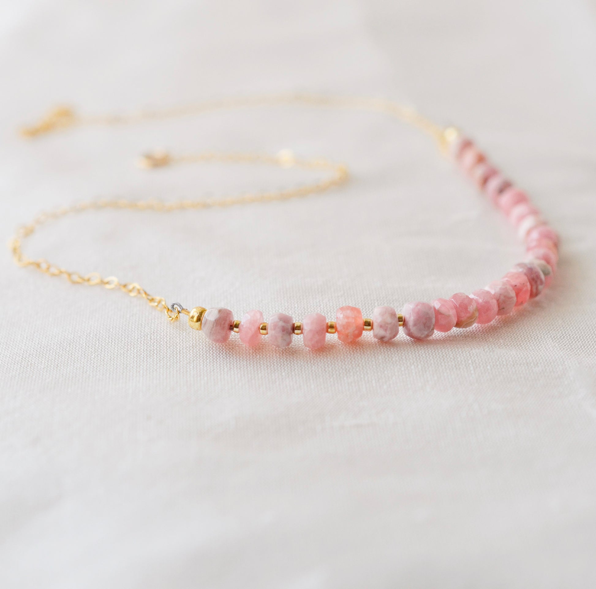 Natural pink Rhodochrosite beaded handmade necklace shown in 14k gold filled. The image is a size view showing the dainty metal beads. The gemstones vary in shades of pink, peach, white, and gray and are faceted rondelle shape. They span approximately 4 inches across the front of the necklace, then attach to a dainty cable chain. Also available in sterling silver.