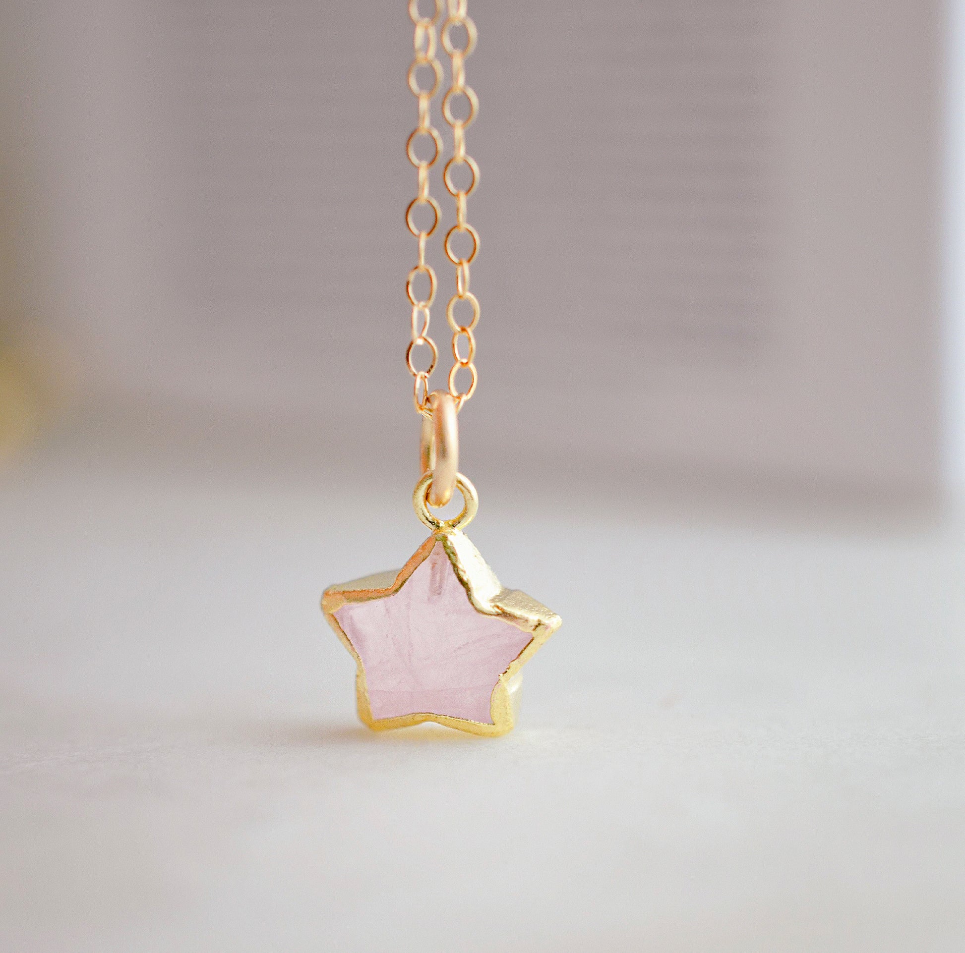 Dainty rose quartz star pendant necklace on a gold chain.
