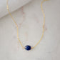 Small blue sapphire stone set onto a gold chain. The stone is a puffed oval shape. 