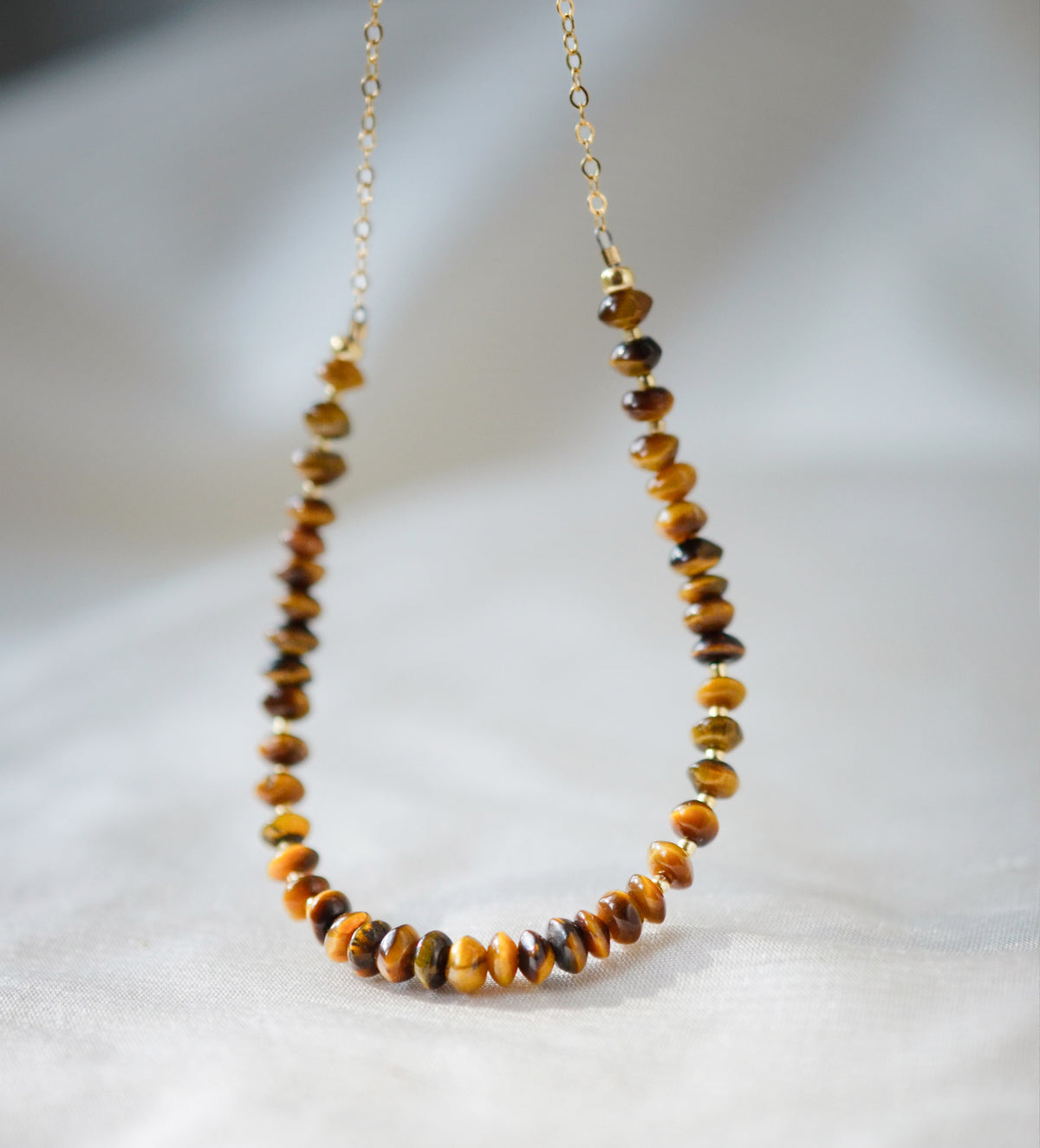 A close up image of genuine brown and gold tigereye gemstones set on a beaded necklace with a 14k gold filled chain. The stones are smooth polished semi-rondelle shape with tiny glass beads in between them. 