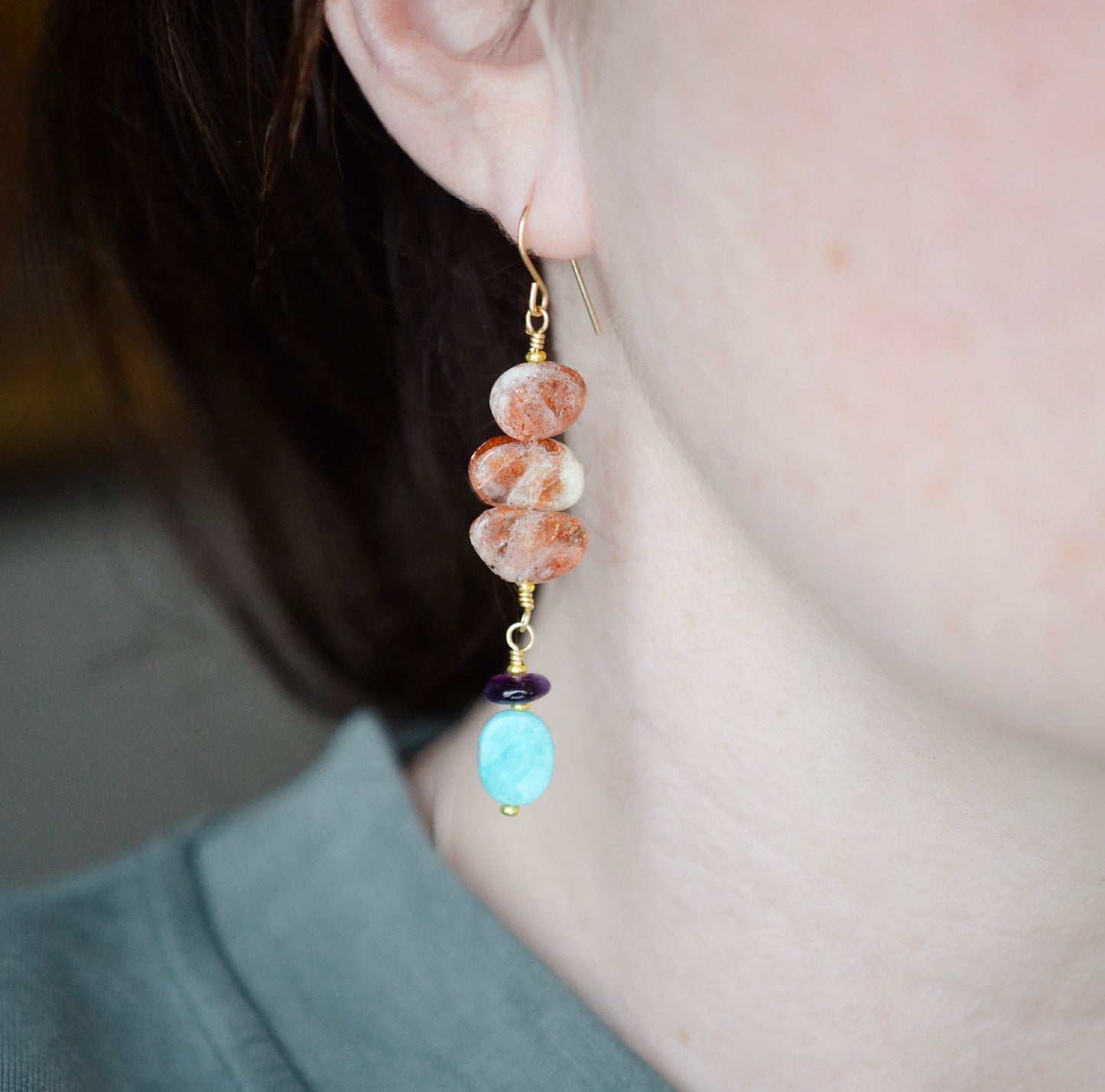 Three sunstone gemstone dangle atop amethyst and amazonite stones. The long earrings are shown in 14k gold filled. Modeled image.
