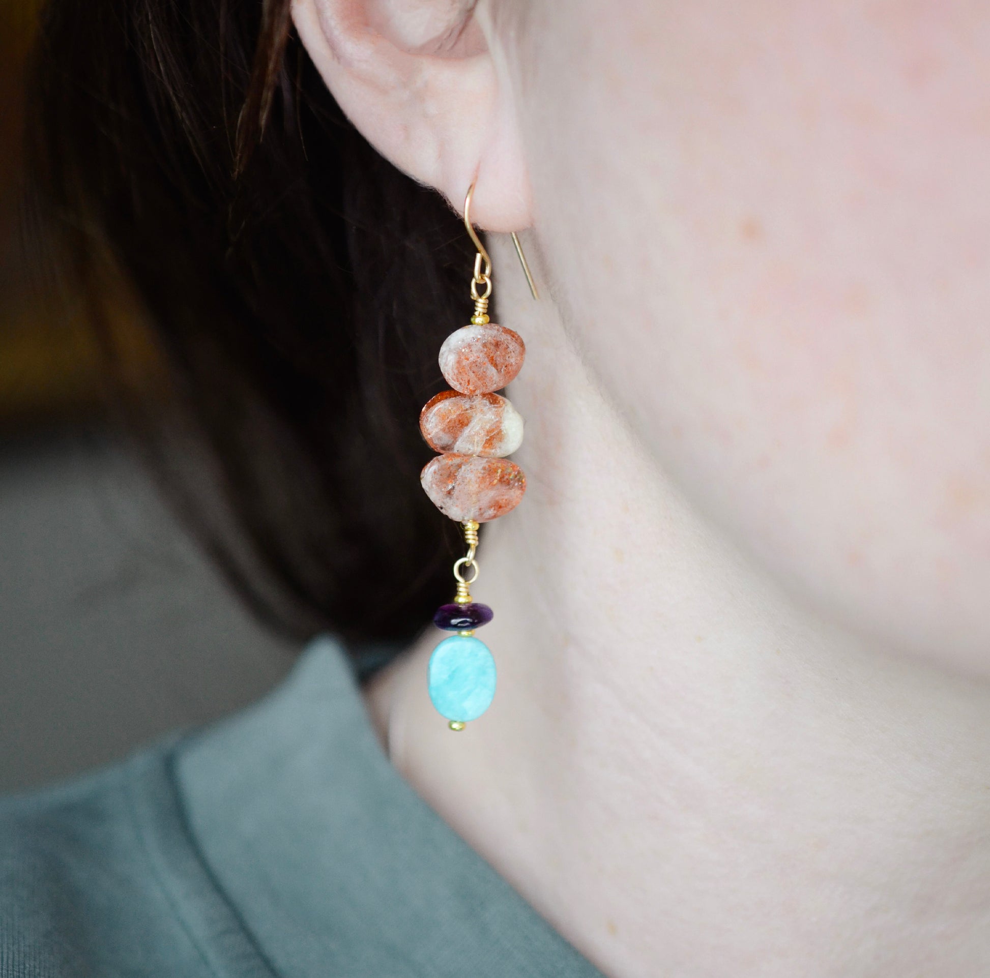 Three sunstone gemstone dangle atop amethyst and amazonite stones. The long earrings are shown in 14k gold filled. Modeled image.
