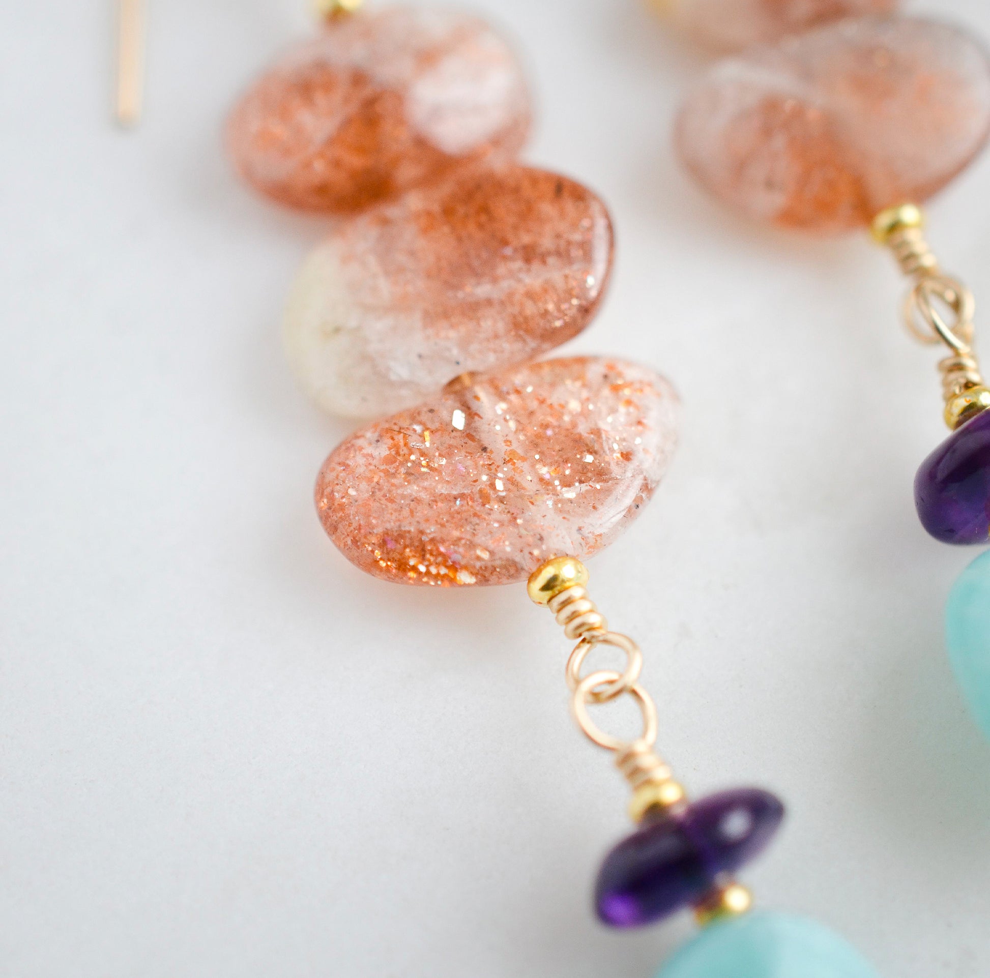 Three sunstone gemstone dangle atop amethyst and amazonite stones. The earring are shown in gold. 