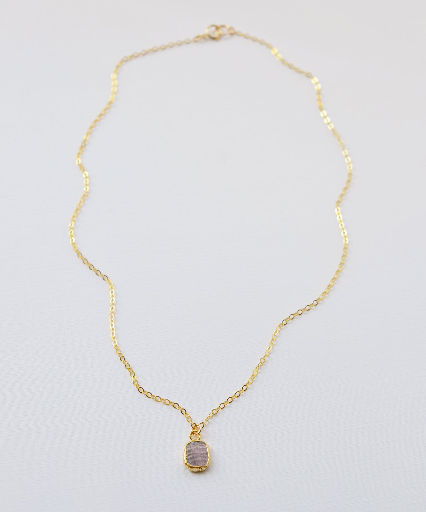 Pale pink Rhodochrosite smooth polished slice set in gold. Shown on a gold chain.