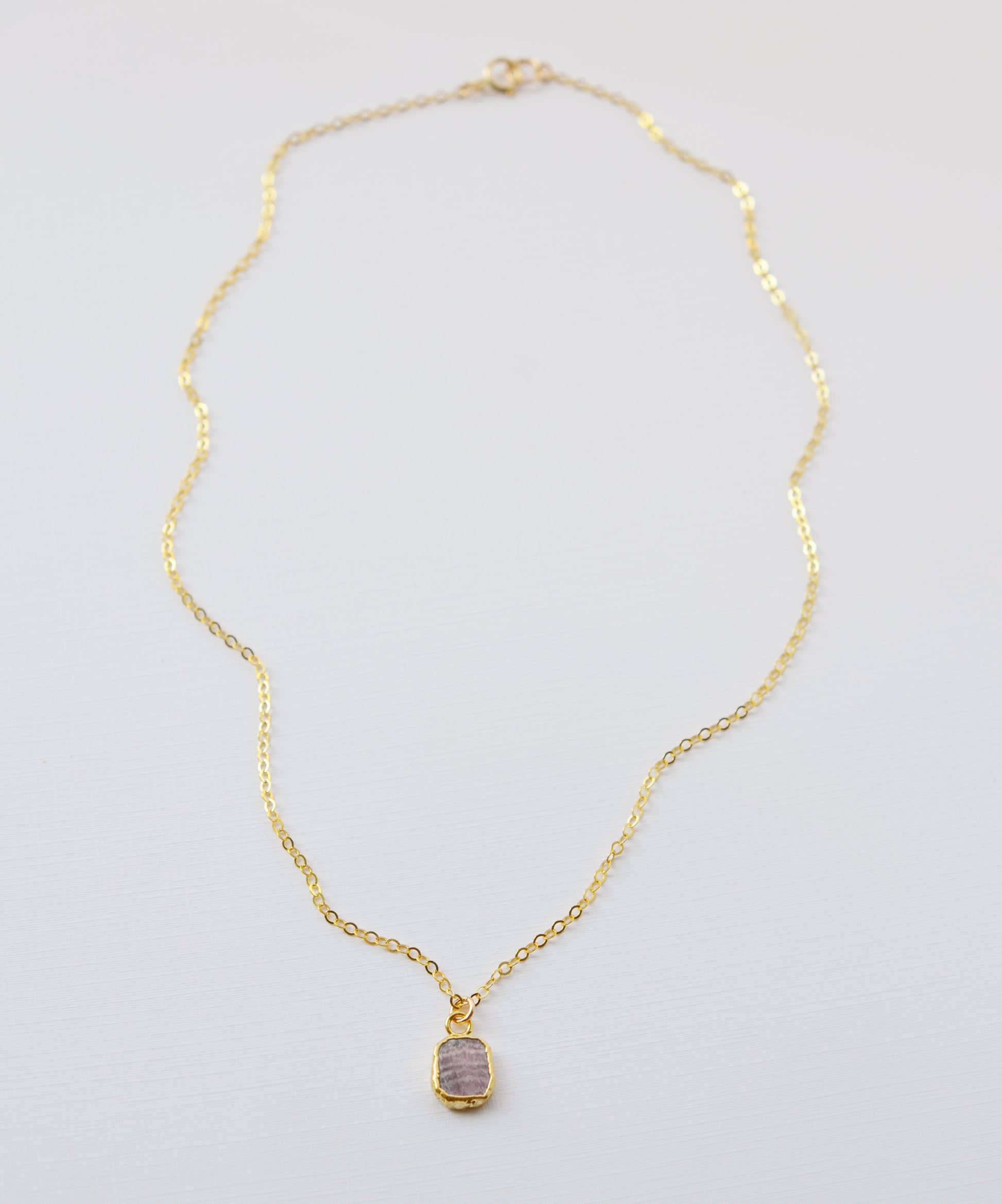 Pale pink Rhodochrosite smooth polished slice set in gold. Shown on a gold chain.