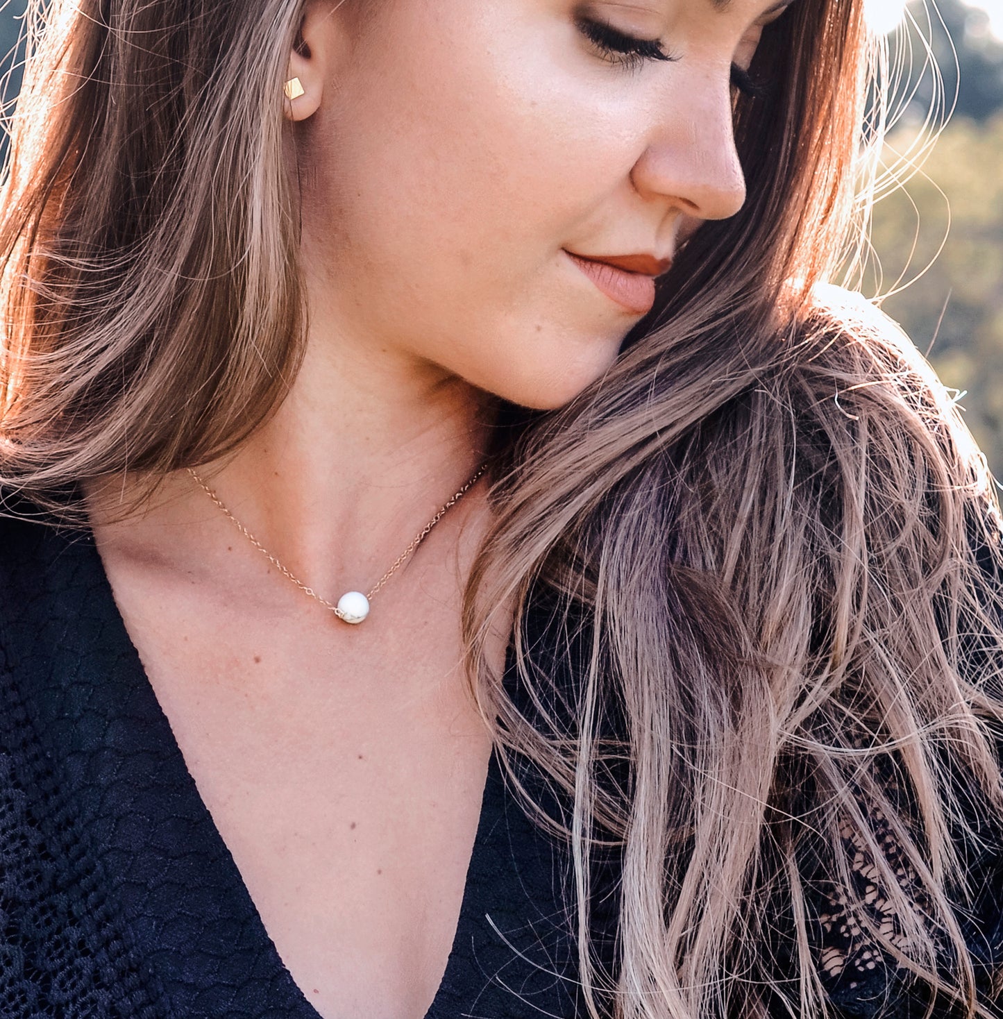 A woman is wearing a natural white howlite necklace. The stone is round with natural gray marbling and set on a 14k gold filled chain. Also available in sterling silver. 
