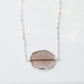 An irregular oval shape, smooth polished Smokey Quartz stone set onto a 14k gold filled chain. The stones edges are raw and irregular. The stone is mostly clear and may show natural inclusions.