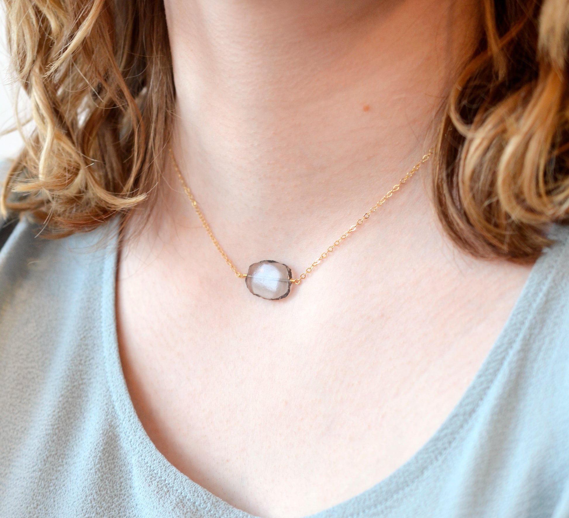 An irregular oval shape, smooth polished Smokey Quartz stone set onto a 14k gold filled chain. The stones edges are raw and irregular. Modeled image.