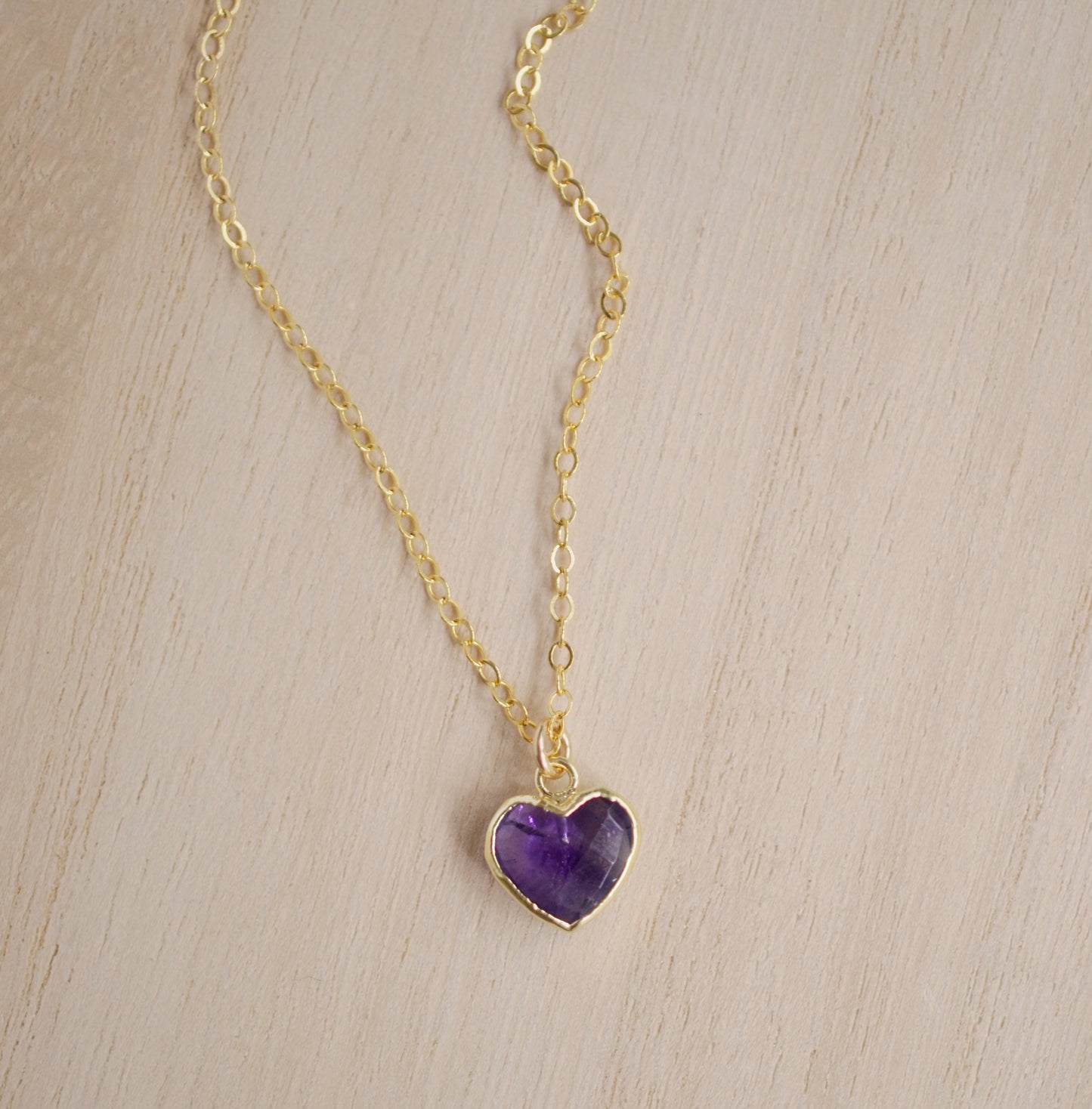 Natural purple amethyst heart stone pendant set onto a gold chain necklace.