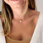 A woman wearing a small white selenite necklace with a single stone. The gemstone is smooth polished and set on your choice of a sterling silver or 14k gold filled chain.