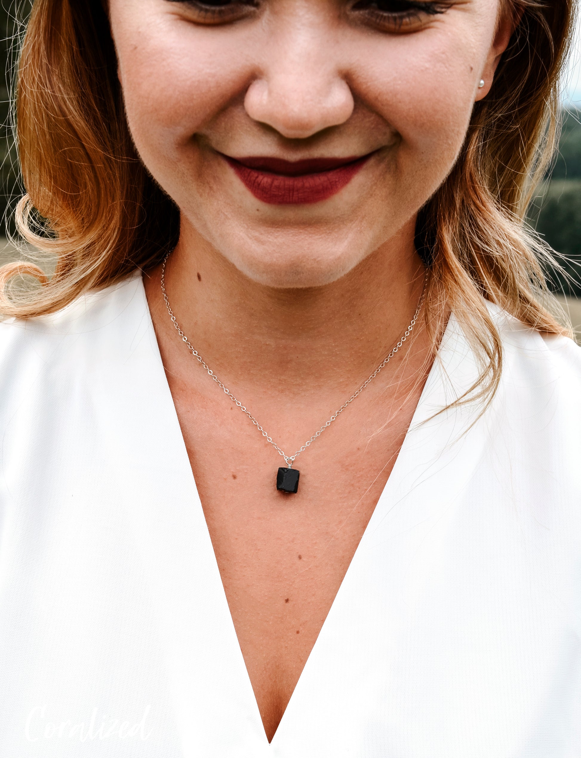 A modeled image of a woman wearing a rough, genuine, black tourmaline crystal necklace in sterling silver. The minimalist jewelry is handmade in Connecticut. 